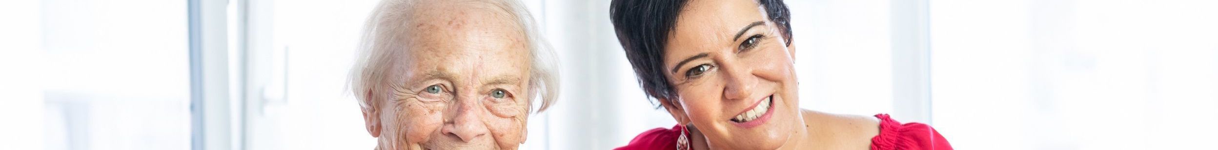 Ältere Frau und Mitarbeiterin der Stiftung lächelnd auf Sofa